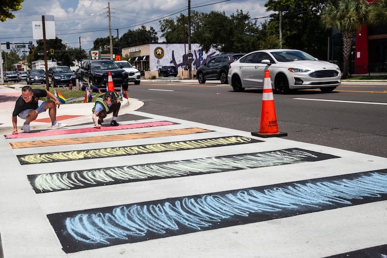 Sen. Carlos Guillermo Smith helps Dallas Perdew color the sidewalk with chalk she brought to bring color back to the intersection in Orlando, Fla., on Thursday, Aug. 21, 2025.