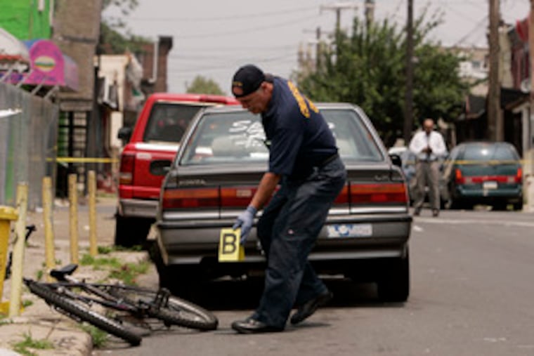 A crime-scene investigator places an evidence marker near a bicycle that police say was used by the gunman who killed Ronald "Sheed" McCorkle at Seventh Street and Tioga Avenue.