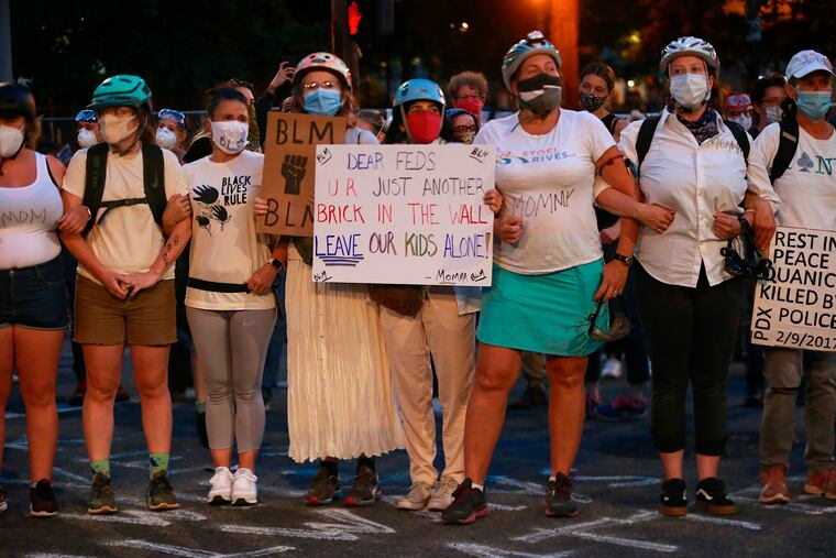 A group of mothers stand arm-in-arm outside the federal building and Justice Center in downtown Portland, Ore., on Saturday, July 18, 2020, during another night of protests in Portland.