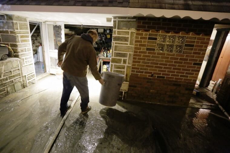 Ed Volmer moves a trash can as water still runs into his basement and garage hours after a large water main burst flooding part of his home on Millbrook Rd. in Phila., PA on January 5, 2017 ELIZABETH ROBERTSON / Staff Photographer 