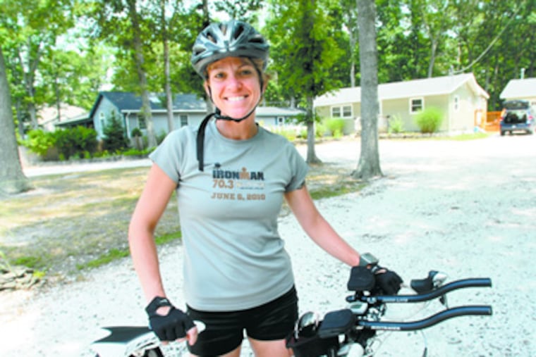 Maria Simone, a Rowan professor who's competing in her first Iron Woman Triathlon in July, stands in front of her home with her bike. ( April Saul / Staff Photographer)