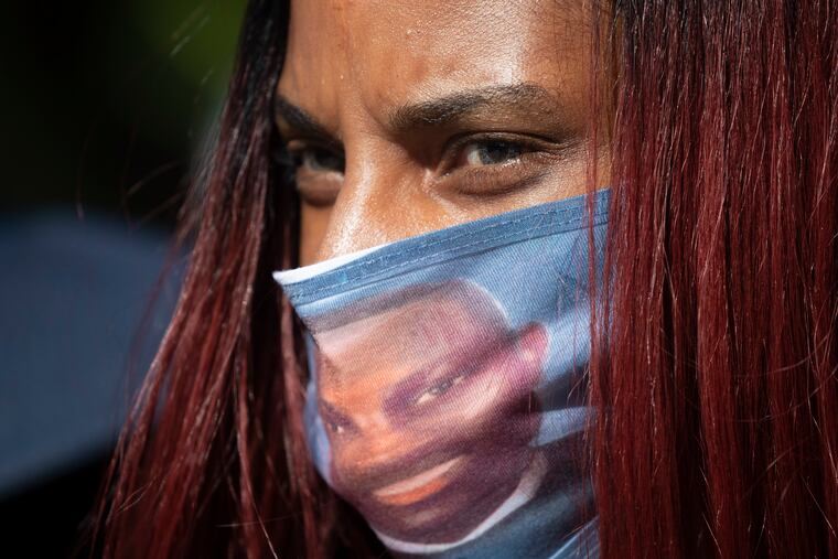 A woman wears a face covering with the likeness of shooting victim Ahmaud Arbery printed on it during a rally Friday to protest Arbery's killing.