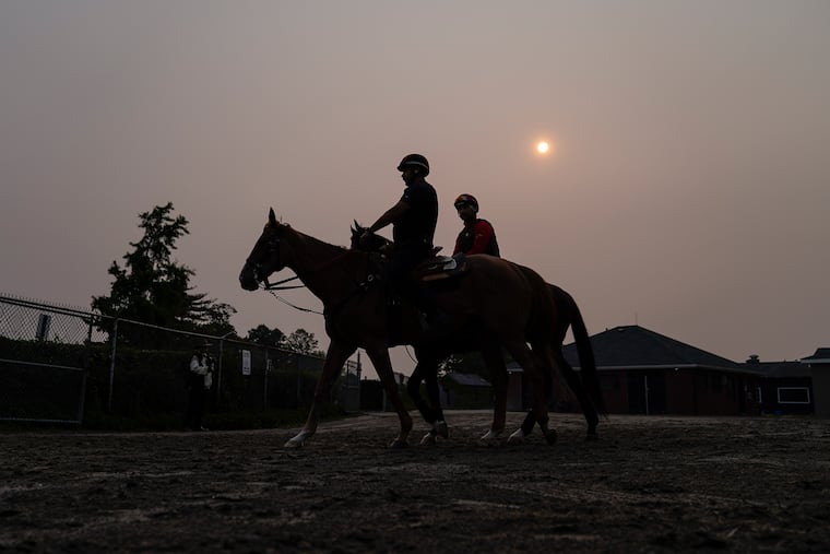 Haze from northern wildfires obscures the rising sun as horsemen ride their mounts toward the track ahead of the Belmont Stakes horse race Wednesday in Elmont, N.Y.