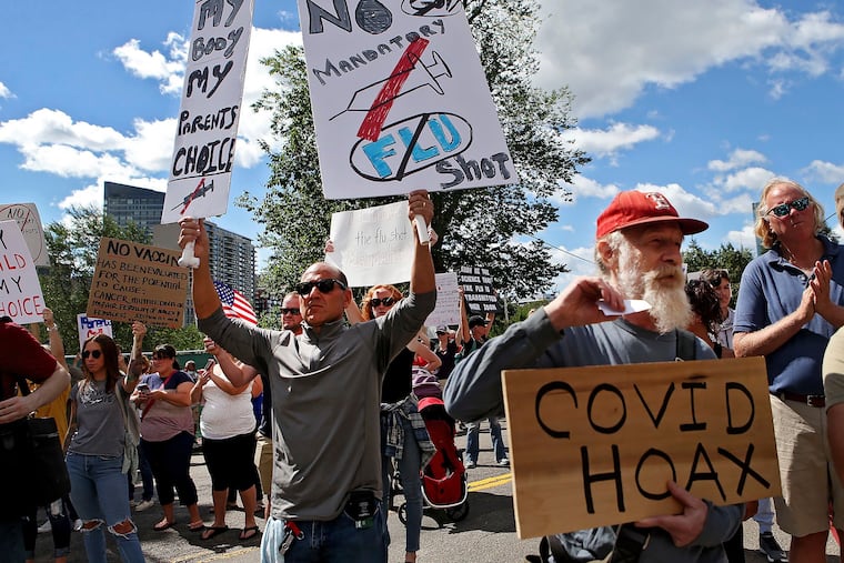FILE - In this Aug. 30, 2020, file photo, Sal Lando, left, of Sterling, holds up signs during a protest against mandatory flu vaccinations, outside the Massachusetts State House, in Boston.