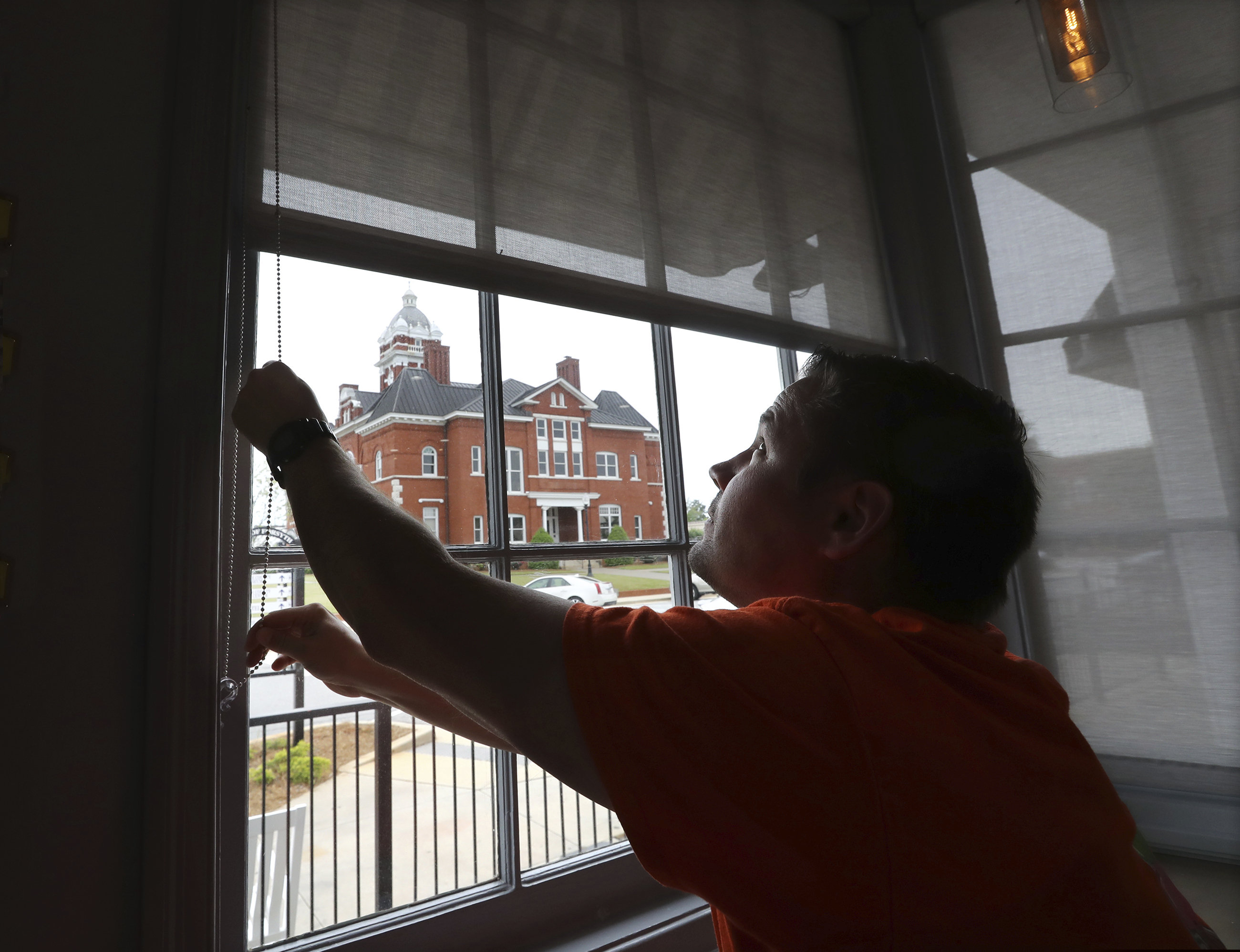Brian Lambert, owner of a coffee and sweets shop in Forsyth, Ga., opens up the windows of his business across the street from the Forsyth Courthouse as he gets ready to reopen next week.