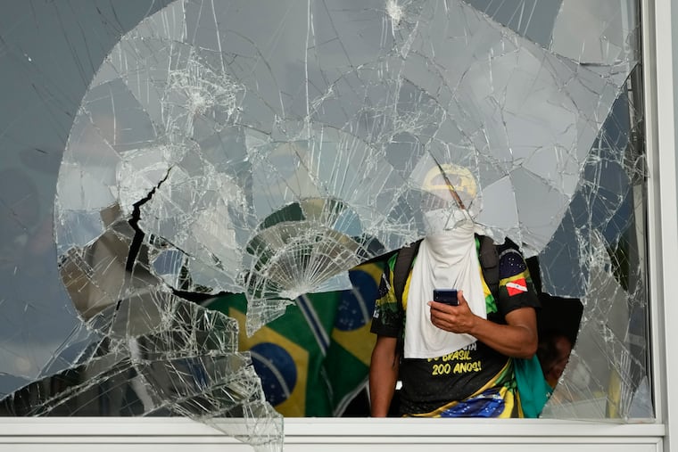 Protesters, supporters of Brazil's former President Jair Bolsonaro, look out from a shattered window after they stormed the Planalto Palace in Brasília, Brazil, on Jan. 8, two years and two days after a similar riot at the U.S. Capitol.