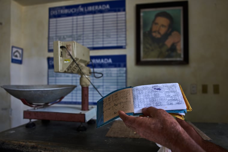 A man shows his ration book, known as a "libreta," backdropped by a framed image of Fidel Castro, at a state-run bodega in Havana, Cuba, Saturday, May 2, 2026.