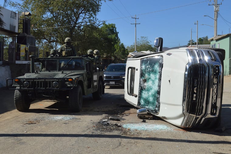 Army soldiers drive past a destroyed vehicle on the streets of Jesus Maria, Mexico, on Saturday, Jan. 7, 2023, the small town where Ovidio Guzman was detained earlier in the week. Thursday's government operation to detain Ovidio, the son of imprisoned drug lord Joaquin "El Chapo" Guzman, unleashed firefights that killed 10 military personnel and 19 suspected members of the Sinaloa drug cartel, according to authorities.