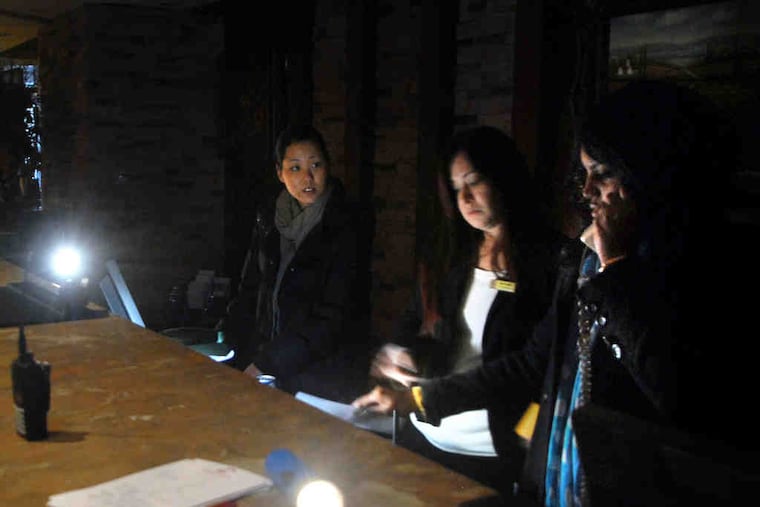 At the front desk of the Crowne Plaza Hotel in Cherry Hill, staffers (from left) Emii Phillips, Carmen Gonzalez, and Diana Berroa work by lantern and flashlight after Tuesday's electrical fire.