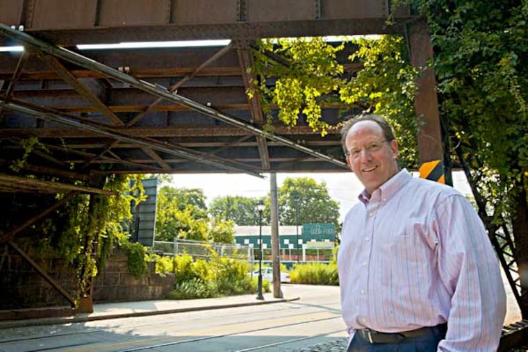 Ken Weinstein stands under an old railroad trestle that is holding up development of the proposed Cresheim Trail which would run near his Trolly Car diner ( in the background) in Mt. Airy. ( RON TARVER / Staff Photographer ) July 23 2014