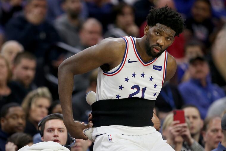 The Sixers' Joel Embiid (21) takes off a back support belt as he prepares to re-enter a game against the Oklahoma City Thunder at the Wells Fargo Center in South Philadelphia on Saturday, Jan. 19, 2019. The Sixers lost 117-115.