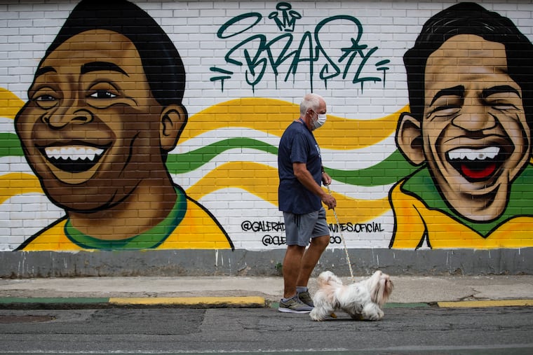 A man walks his dog past a mural of Brazilian soccer stars Pelé (left) and Garrincha in Rio de Janerio on Friday.