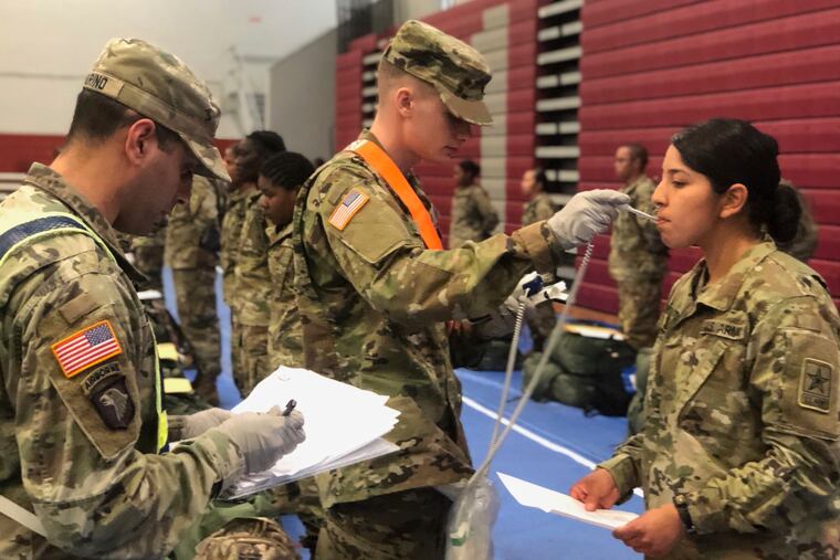 In this image provided by the U.S. Army, recent Army basic combat training graduates have their temperatures taken as they arrive at Fort Lee, Va.