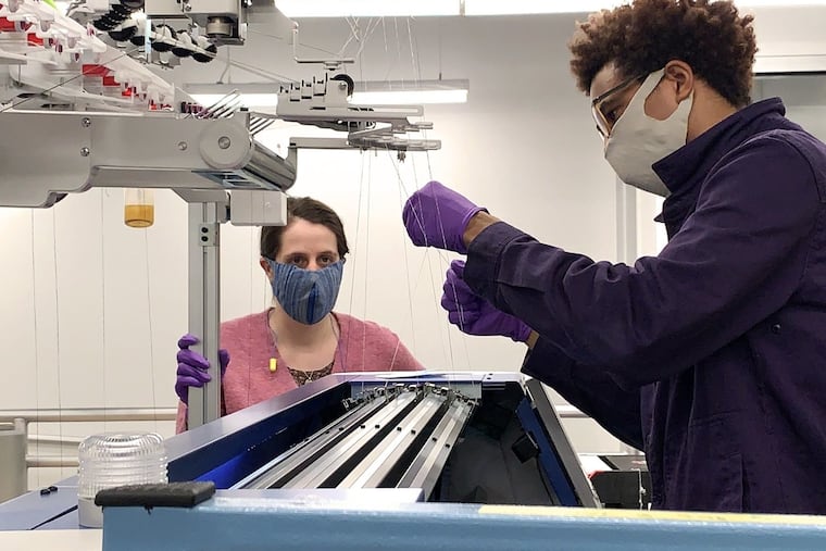 Chelsea Amanatides, left, and Keith Taylor, both textile fabrication technicians, on Tuesday, March 24, 2020, work at one of the Shima Seiki weft knitting machines used to make the masks they are wearing at the Pennsylvania Fabric Discovery Center at Drexel University.