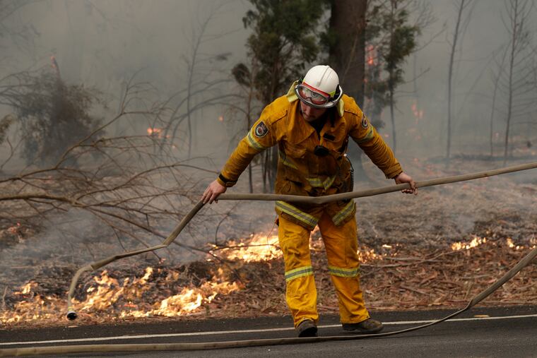 A firefighter battles a fire near Burrill Lake, Sunday, Jan. 5, 2020. Milder temperatures Sunday brought hope of a respite from wildfires that have ravaged three Australian states, destroying almost 2,000 homes. (AP Photo/Rick Rycroft)
