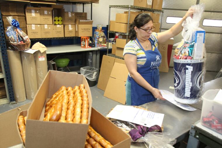 Diana Mendoza of the Pennsylvania General Store is shown getting a Penn State gift basket together in their new warehouse space in Feltonville. Pennsylvania General Store began as a small stand within the Reading Terminal Market in 1987 selling locally made specialty foods, evolved into a mail-order company whose reach got even farther thanks to the Internet. It has now moved its offices to Feltonville for more space and better shipping access. (CHARLES FOX / Staff Photographer)