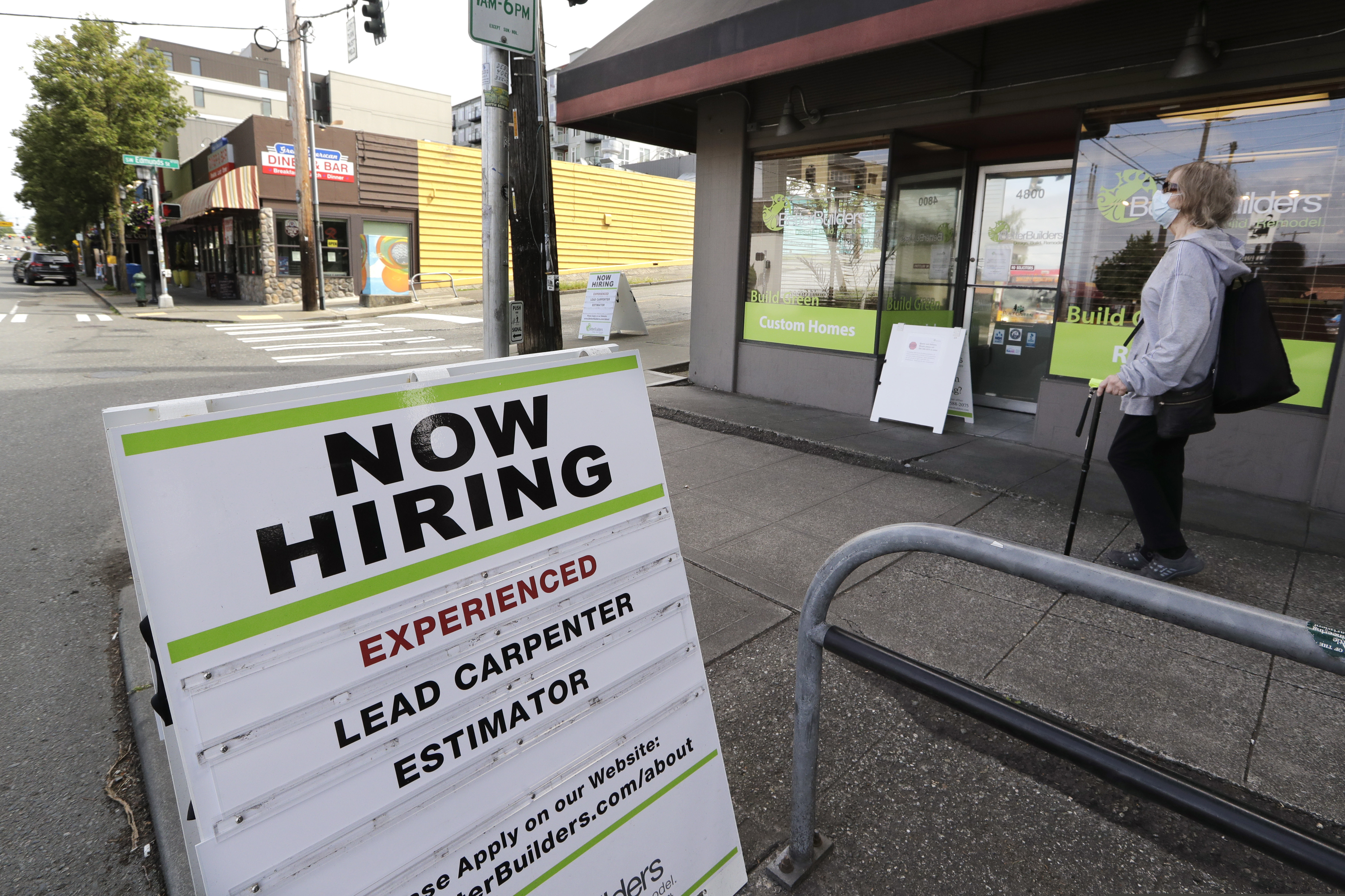 In this photo taken Thursday, June 4, 2020, a pedestrian wearing a mask walks past reader board advertising a job opening for a remodeling company, in Seattle. The U.S. unemployment rate fell to 13.3% in May, and 2.5 million jobs were added — but the rate was underestimated by 3 points due to the way the numbers were collected. (AP Photo/Elaine Thompson)