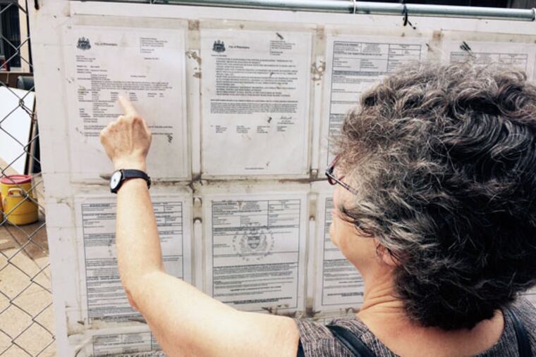 Feet First Philly co-chairwoman Debby Schaaf checks the expiration date of a permit posted at a construction site near 18th and Arch streets. (STU BYKOFSKY/DAILY NEWS STAFF)
