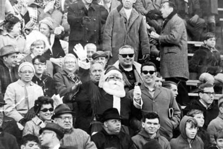 Shown in this 1967 copy photograph is Eagles fan Frank Olivo, center, wearing his Santa suit in the stands of an Eagles game at Franklin Field in 1967. Olivo was the Santa who was booed and dodged snowballs during halftime at a 1968 Eagles game. (AP Photo)