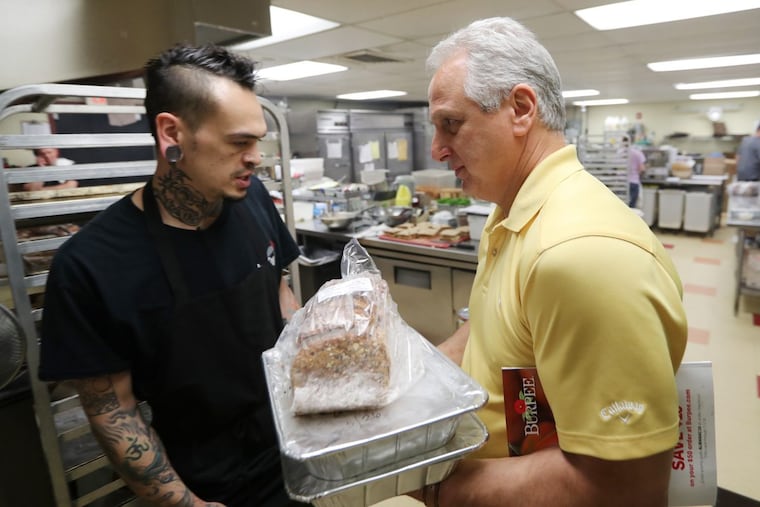 Bob Ventresca (right), of Bucks County Food Runners, gathers beef lasagna and sides from chef David Demko at the Delaware Valley College Farm Market in Doylestown for delivery to a women’s shelter.