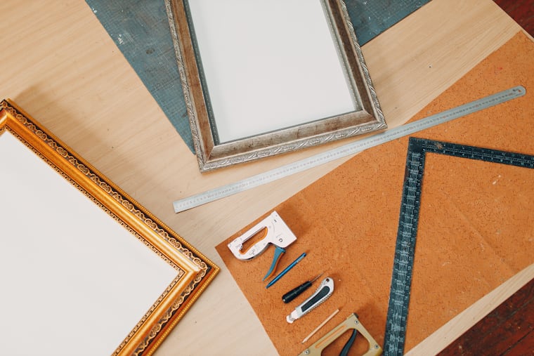 A framing workshop with stapler, ruler, and frames at a studio table. Delaware Valley Consumers’ Checkbook compared pricing and offered services of various options for framing art and photos.