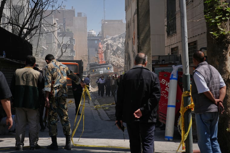 Bystanders watch from a distance as rescue teams and first responders work at the site of a strike that, according to a security official at the scene, destroyed half of the Khorasaniha Synagogue and nearby residential buildings in Tehran, Iran, Tuesday, April 7, 2026.