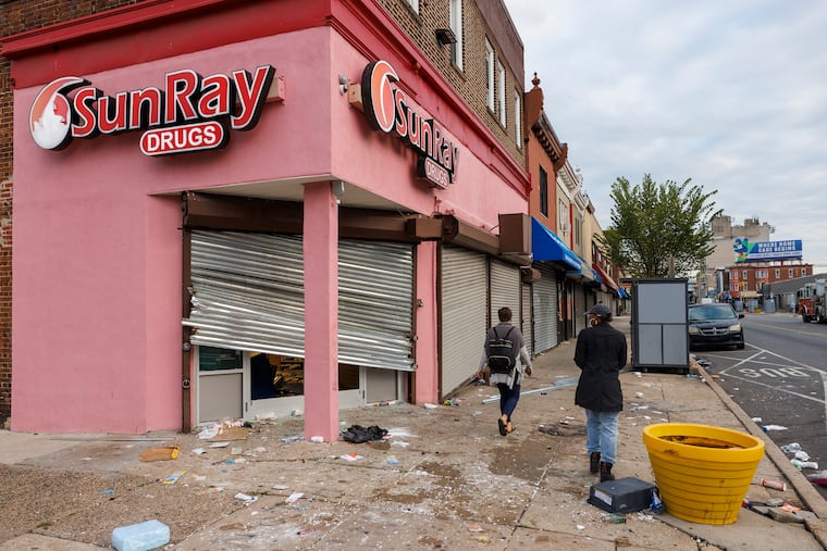 Pedestrians navigate the damage from vandalism at South 52nd and Walnut Streets on Wednesday. The unrest stretched across the city, including Center City, the Northeast, and West Philadelphia, with business corridors along Aramingo Avenue and Walnut Street targeted through the night.