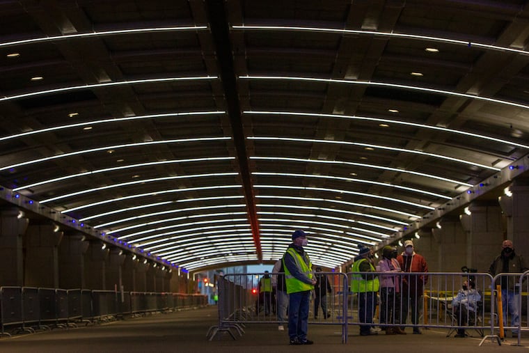 FEMA worker standing along N.12th St under the lights above the street as registered Philadelphians wait for entry into Pennsylvania Convention Center for COVID-19 vaccine at the FEMA's mass vaccination clinic on Wednesday morning March 18, 2021.