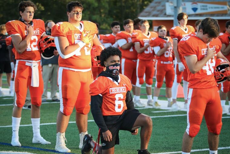 Cherokee senior football captain Darnell Hightower takes a knee during the national anthem before Friday night's season opener vs. Pennsauken.