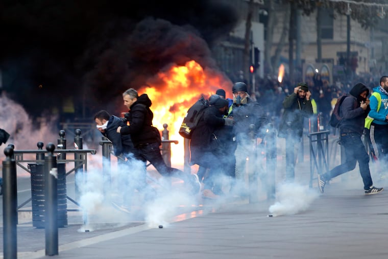 People run away from a burning car during clashes, Saturday, Dec. 8, 2018 in Marseille, southern France. The grassroots movement began as resistance against a rise in taxes for diesel and gasoline, but quickly expanded to encompass frustration at stagnant incomes and the growing cost of living.