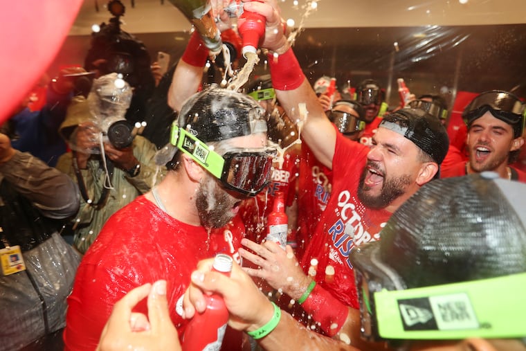 Phillies designated hitter Bryce Harper gets doused with champagne and beer from teammate Kyle Schwarber after the Phillies clinched an NLDS berth earlier this month.