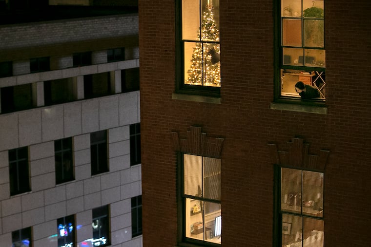 The holidays pose special challenges for isolation. Anna Evenosky, 22, looks out of her apartment window on Walnut Street in November when the physical therapy grad student was home to quarantine after she was exposed to COVID-19 by a lab partner, She put up the tree to keep her spirits up.