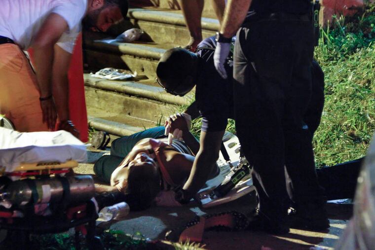 A paramedic from the Philadelphia Fire Department holds the hand of a woman who was run over by a car on the 900 block of Anchor Street in the Summerdale section of Philadelphia on Saturday, July 6, 2013. (For the Daily News/ Joseph Kaczmarek)