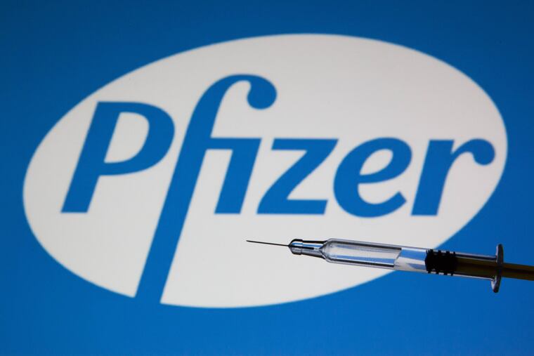 In a photo illustration, a medical syringe is seen displayed in front of Pfizer's logo.