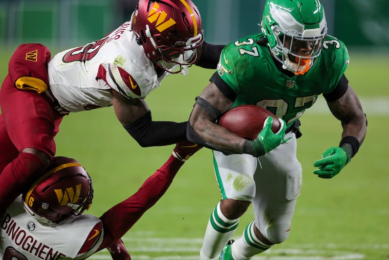 Commanders defensive backs Noah Igbinoghene and Jeremy Reaves try to bring down Eagles running back Tank Bigsby on a third-quarter run on Sunday at Lincoln Financial Field.