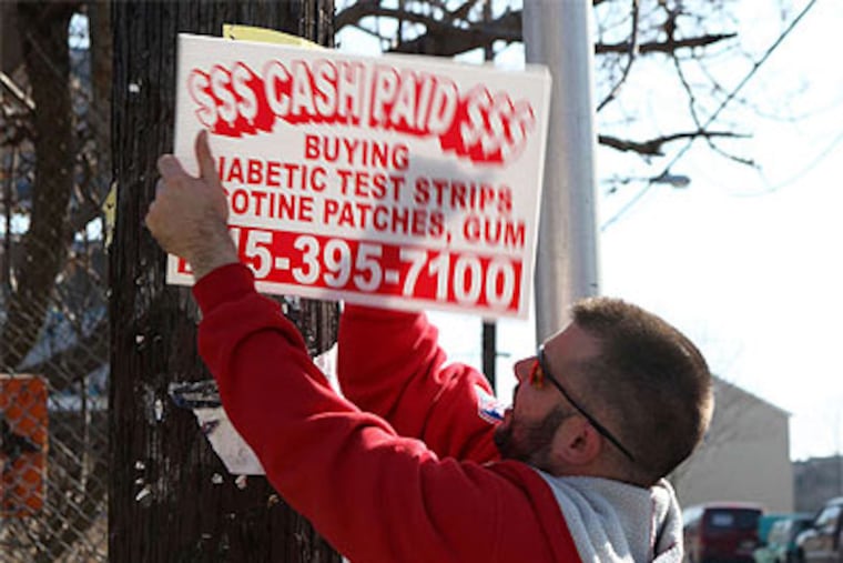 Christopher Sawyer removes a 'bandit' sign at 6th Street and Montgomery Avenue. (Kate McCann / Staff Photographer)