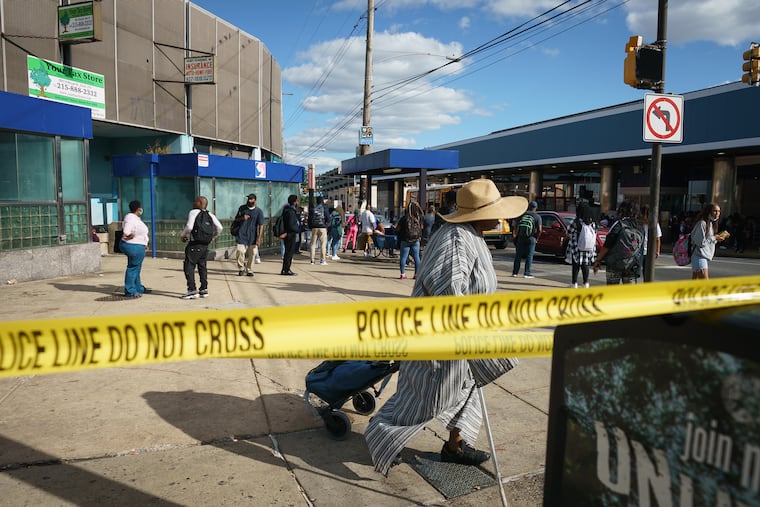 Commuters walk past crime scene tape at Broad Street and Olney Avenue, one block away a shooting that left one person dead and five wounded on Monday.