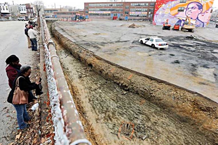 Women view unearthed caskets behind William Dick Elementary School, Thursday, Dec. 5, 2013, in Philadelphia. Philadelphia Water Department crews doing excavation work behind the school on Wednesday afternoon unearthed several coffins and headstones. The city Department of Licenses and Inspections and the Historical Society have been called in to figure out how old they are and determine if remains are still present. (AP Photo/Matt Rourke)