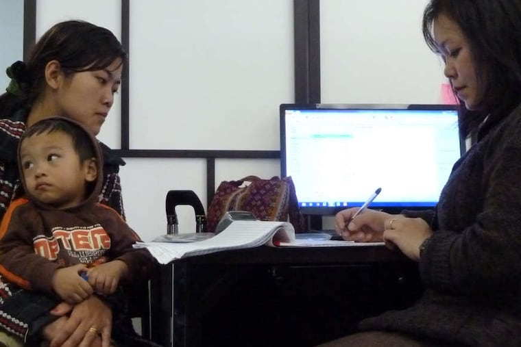 Biak Sung gets help from Zing Thluai (right), an outreach worker for Seamaac, a nonprofit organization in South Philadelphia. A lack of access to the Internet has hampered the group's clients.