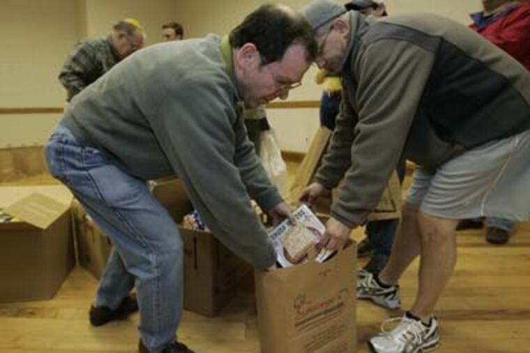 Harold Bernheim (left), a volunteer for Temple Sinai, puts a box of matzo in a bag. Project H.O.P.E. is delivering meals to Jewish families in the region. (Michael Bryant / Staff Photographer)
