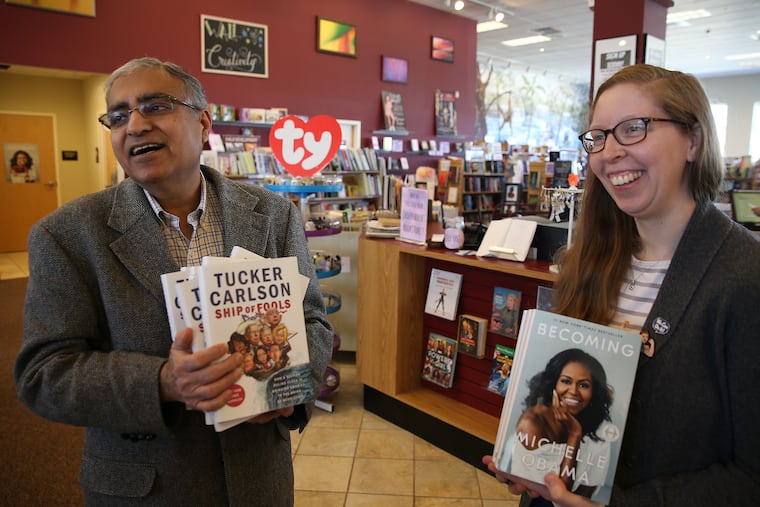 Owner P.K. Sindwani, left, carries a stack of "Ship of Fools" by Tucker Carlson, as assistant manager and book buyer Sarah Danforth, holds a bunch of "Becoming" by Michelle Obama at Towne Book Center & Wine Bar in Collegeville, PA on March 26, 2019.