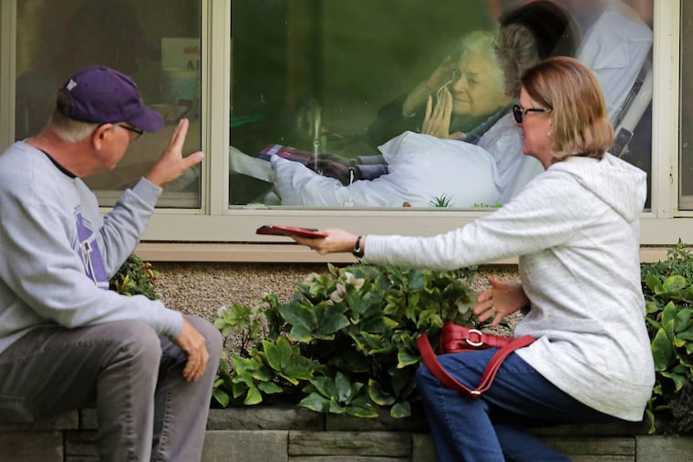 Judie Shape, center, who has tested positive for the coronavirus, blows a kiss to her son-in-law, Michael Spencer, left, as Shape's daughter, Lori Spencer, right, looks on, Wednesday, March 11, 2020, as they visit on the phone and look at each other through a window at the Life Care Center in Kirkland, Wash., near Seattle. In-person visits are not allowed at the nursing home. The vast majority of people recover from the new coronavirus.
