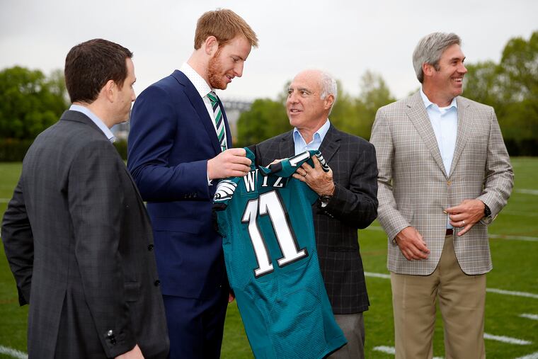 Eagles first round draft pick Carson Wentz, holds his jersey with Eagles owner and chairman Jeffrey Lurie in April 2016. Howie Roseman is on the left, and coach Doug Pederson on the right.