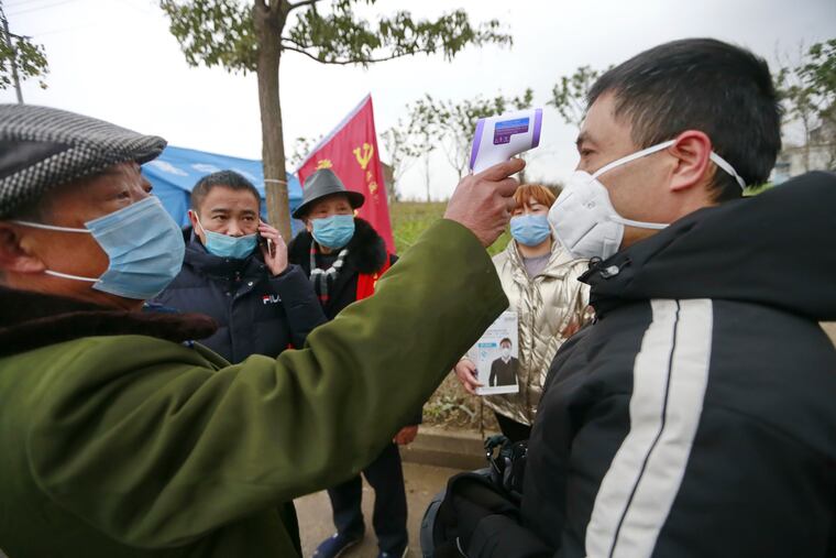 In this Saturday, Feb. 1, 2020, photo, a government worker takes the temperature of a passer-by at a checkpoint in Suining in southwestern China's Sichuan Province. China's death toll from a new virus has increased to 304 with more than 14,000 cases, amid warnings from the World Health Organization that other countries need to be prepared in the event the disease spreads among their populations.