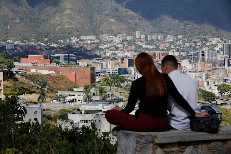 A couple sits on a bench at a viewpoint overlooking the U.S. embassy, center left, in Caracas, Venezuela, Friday, Jan. 9, 2026. (AP Photo/Cristian Hernandez)