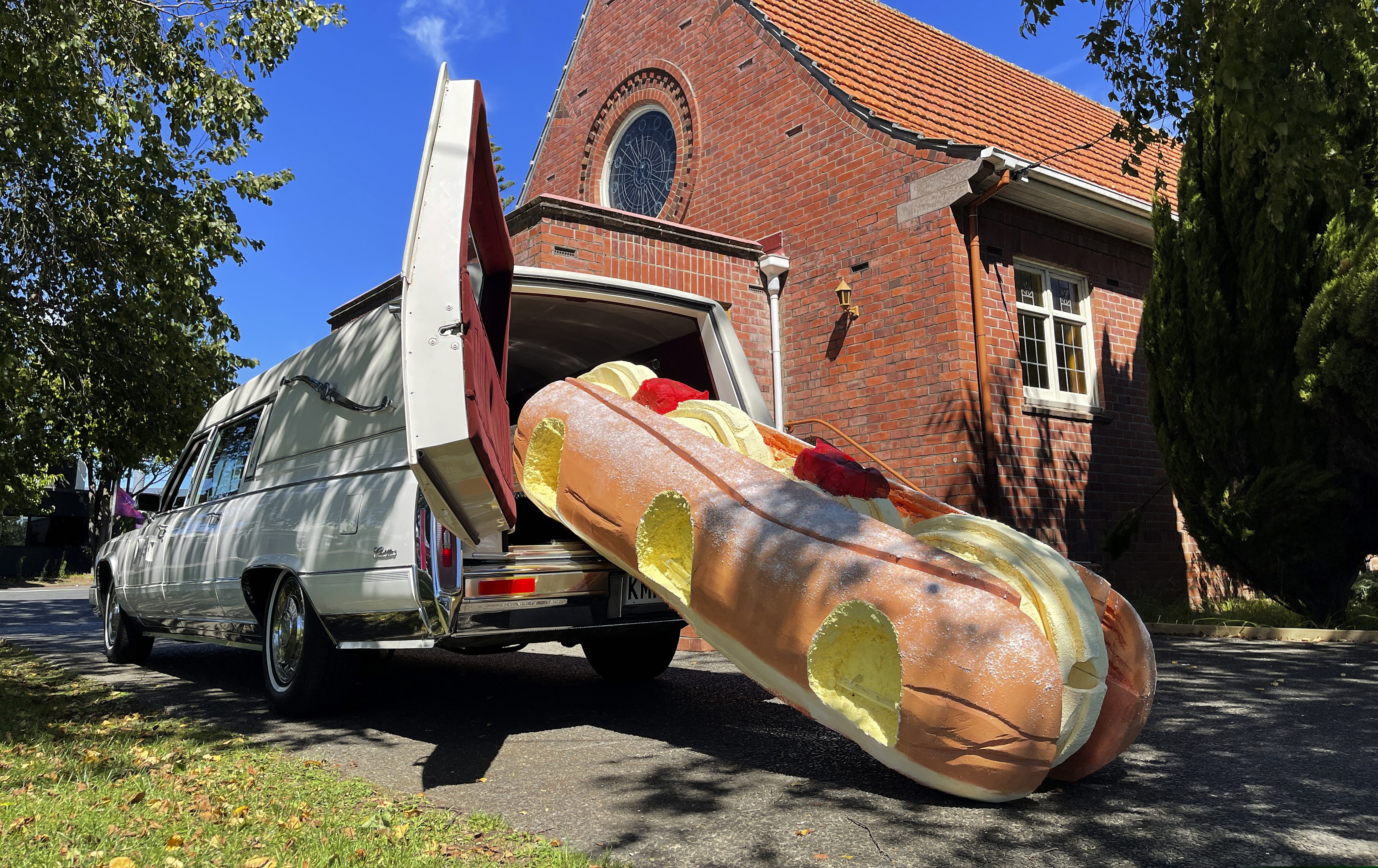 This photo provided by Ross Hall, shows a cream doughnut shaped coffin for the funeral of Phil McLean outside a church in Tauranga, New Zealand on Feb 17, 2021. Auckland company Dying Art makes unique custom caskets which reflect the people who will eventually lay inside them, whether it's a love for fire engines, a cream doughnut or Lego. (Ross Hall via AP)