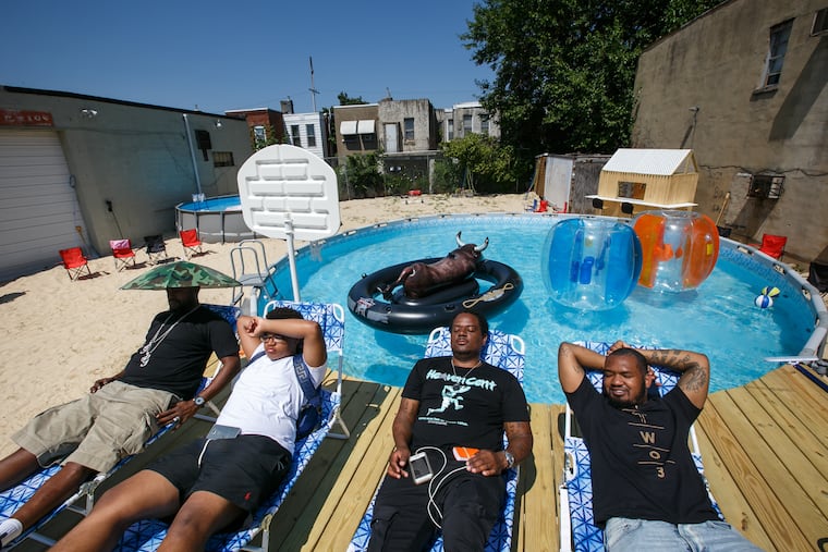 (Left to Right) Disco Inferno (nickname), Tariq Knight, his father and the owner of the lot, Chris Knight, and the promotor of the space, David Brown, relax poolside, this former parking lot in North Philly has been converted into a mini beach with sand, above ground pools, a wooden deck and beach furniture, in Philadelphia, Wednesday, July 11, 2018. This site will be the setting of an upcoming pool party.