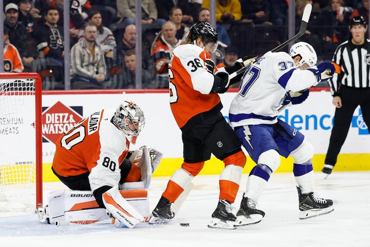 Flyers goaltender Dan Vladar (left) looks down at the loose puck as teammate defenseman Emil Andrae defends Lightning's Yanni Gourde during the second period.