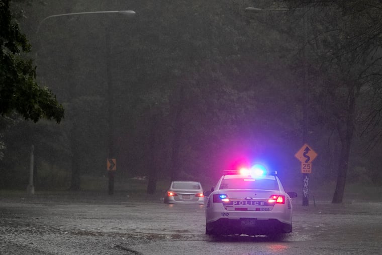 Philadelphia police officer blocks the roadway along Cobbs Creek Parkway as a vehicle sits in flood water near Springfield Ave in Philadelphia during heavy rain on August 4.