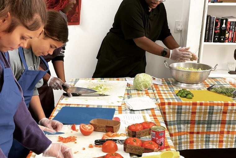 William Brown (center) preps vegetables with other teenagers during the Philly Bridge & Jawn pilot program in November. The nonprofit program pays teenagers a stipend to come together and cook meals for one another.